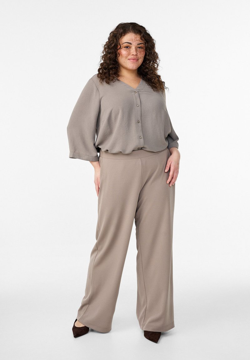 Bež bluza z zaobljenim izrezom in gumbi, kombinirana z visokim pasom hlač v enakem gladkem, tekočem materialu.