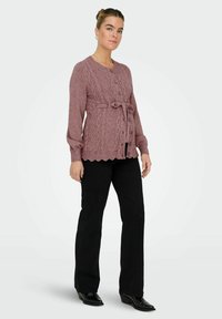 Adīts kardigans mauve krāsā ar kabeli rakstu, pogu aizdari un loku detaļu. Kombinēts ar melniem platiem biksēm un augstpapēžu zābakiem.