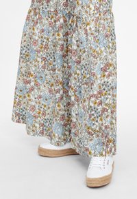 Jupe longue fleurie avec des fleurs bleues, jaunes et roses portée avec des baskets espadrilles blanches à plateforme sur fond blanc.