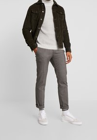Chaqueta de pana verde oscuro, suéter de canalé gris claro, pantalones grises a medida y zapatillas blancas con calcetines de rayas en blanco y negro.