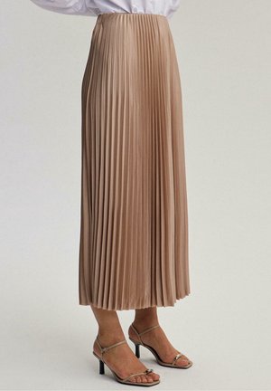 Jupe midi plissée beige portée avec des sandales à talons beige à lanières et un chemisier blanc rentré, montrée de la taille aux pieds sur un fond neutre.