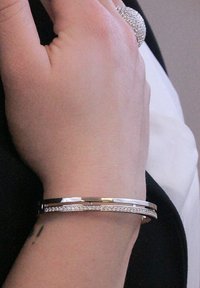 Bracciale in argento con due sezioni collegate; una presenta una fila di piccoli cristalli trasparenti. Finitura in metallo liscia, design elegante.