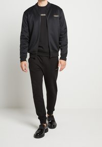 Chándal casual negro con una chaqueta bomber y pantalones a juego. Tejido suave con un diseño minimalista; cuenta con acentos de logo en tonos oscuros.