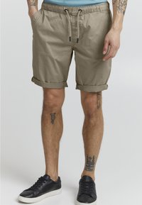 Beige shorts med elastisk talje og justerbar snor. Har opsmøgede kanter og sidelommer. Bæres med sorte sneakers.