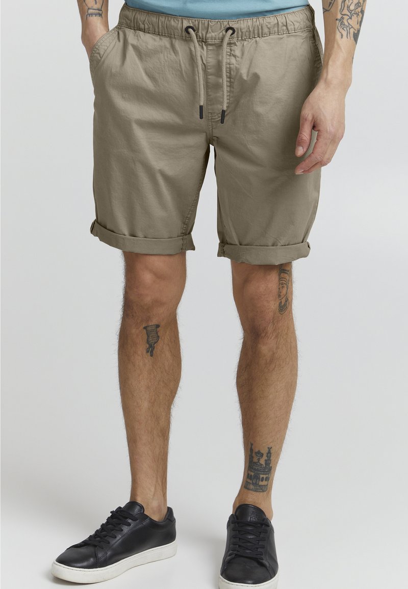 Beige shorts med elastisk talje og justerbar snor. Har opsmøgede kanter og sidelommer. Bæres med sorte sneakers.
