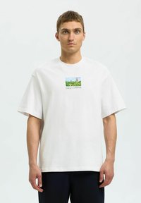 Biała bawełniana koszulka z krótkim rękawem, z małą kolorową grafiką krajobrazu na piersi. Prosty dół i luźny krój.