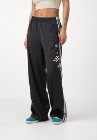 Svarta satinbyxor med bred passform, med vita sidostreep och blommig brodering på höger ben. Elastisk midja för bra passform.