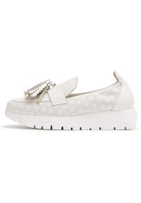 Zapato blanco tipo slip-on con parte superior de cuero texturizado, diseño perforado, banda elástica y acento metálico. Cuenta con una suela blanca gruesa.