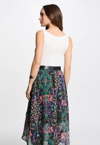 Sleeveless white top paired with a long, sheer skirt featuring a colorful floral and animal print in green, purple, and pink tones.
