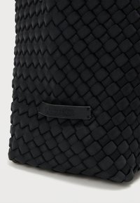 Μαύρη υφασμάτινη τσάντα με υφαντό, υφή και διακοσμητικό μοτίβο. Διαθέτει μικρή ετικέτα με το όνομα της επωνυμίας.