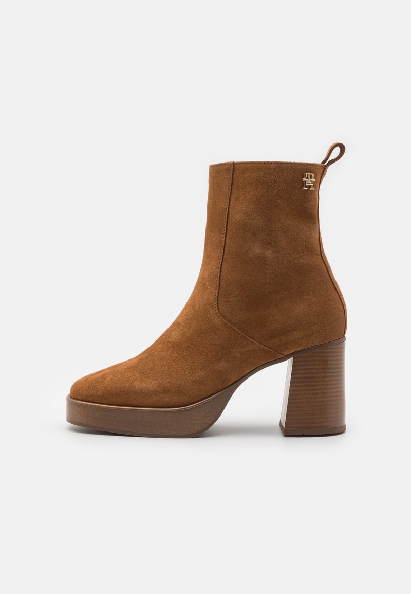 Bottine en daim marron avec talon bloc, bout arrondi et petite bride de tirage. Présente un logo subtilement embossé sur le côté.