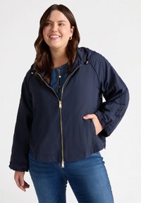 Granatowa lekka kurtka z kapturem, z zapięciem na zamek i bocznymi kieszeniami. Posiada teksturowane wykończenie oraz elastyczne mankiety z elementami w kolorze złotym.