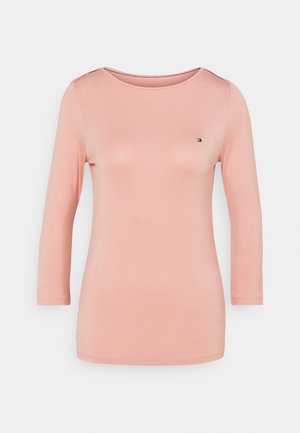 Jasnoróżowy damski top z długim rękawem, okrągłym dekoltem i małym logo Tommy Hilfiger na lewej piersi.