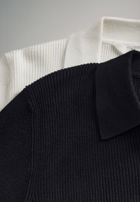 Zwart-witte geribbelde gebreide polo's in lagen, met kraag en schoudergedeelten zichtbaar op een effen lichte achtergrond.