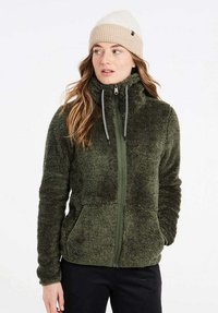 Fuzzy groene fleecejas met hoge kraag, volledige rits, twee zijzakken en verstelbare trekkoorden. Gecombineerd met een lichtbeige gebreide beanie.