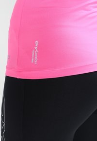 Rosa Sporttop mit körpernahem Schnitt, aus feuchtigkeitstransportierendem Material, mit Logostickerei. Kombiniert mit schwarzen Leggings.