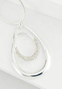 Silberne Halskette mit einem ovalen Anhänger mit polierter Oberfläche und einem kleineren inneren Oval, das mit kleinen klaren Kristallen verziert ist.