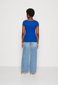 Blue ribbed short-sleeve top paired with wide-leg light denim jeans. The top has a round neckline and fitted design.
