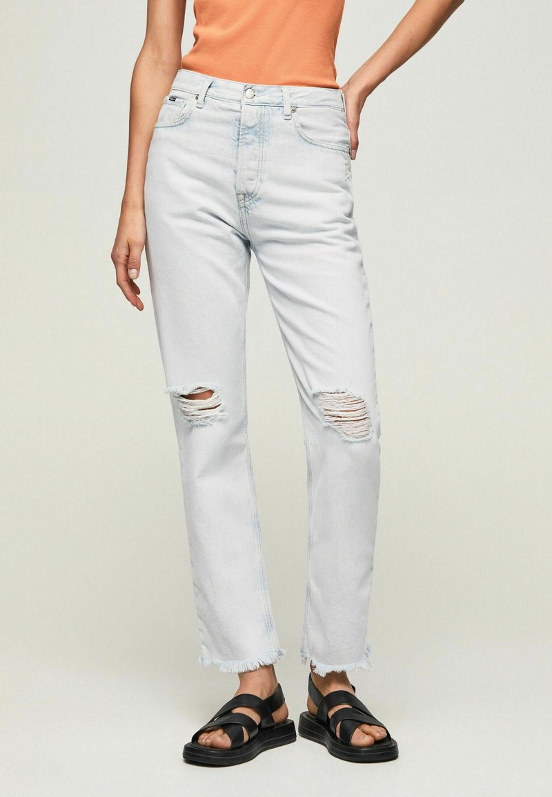 Helle blaue, zerissene Jeans mit geradem Bein, versehen mit ausgefransten Säumen und sichtbaren Nähten. Kombiniert mit schwarzen Sandalen.
