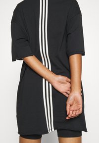 Camiseta negra oversize con rayas verticales blancas en el centro, de mangas cortas y un corte relajado. Manos colocadas detrás de la espalda.