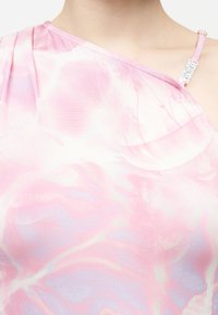 Εγγύς πλάνο ενός ατόμου που φοράει ροζ και άσπρο τοπ με δεσίματα τύπου tie-dye και ακάλυπτους ώμους, με λεπτό ιμάντα που φέρει την ετικέτα "Juicy Couture".