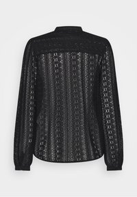 Blouse en dentelle noire à manches longues avec des motifs floraux, poignets à boutons et col montant, présentée de dos sur un fond uni.