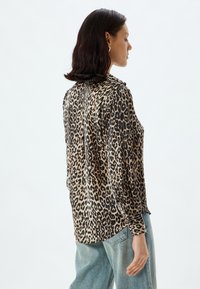 Blouse imprimé léopard en tissu léger, avec un col et un devant à boutons. Manches longues resserrées aux poignets ; coupe décontractée.