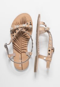 Sandalias de cuero beige con tira en el tobillo, decoradas con conchas y tachuelas metálicas, y estampado de hojas de palma en las plantas.