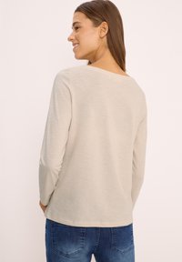 Light beige long-sleeve top with a wide neckline, soft texture, and a relaxed fit, paired with blue denim jeans.