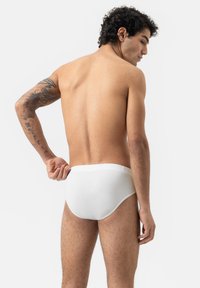 Caleçons en coton blancs avec une taille lisse et plate. Le modèle a les cheveux courts et bouclés, et des tatouages visibles sur le bras gauche.