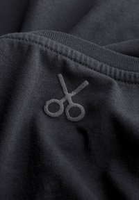 Detailopname van zwart stof met een gestikt schaarontwerp in iets lichter grijs garen, met een soepele textuur en subtiele ribbelranden.