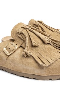 Tan suede instappers met franjes, een gouden gesp en een gerubberde zool, wat zorgt voor een zachte en casual uitstraling.