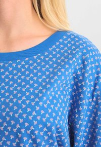 Blå kortärmad topp med rund halsringning, prydd med ett blommönster i rosa och ljusblått på en texturerad tyg.