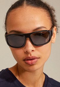 Black oversized sunglasses with dark lenses, thick rectangular frames, and a glossy finish. No prominent logos or patterns visible.