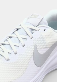 White athletic shoe with textured upper, featuring light gray Nike swoosh, lace-up design, and smooth sole. Subtle blue accents visible inside.