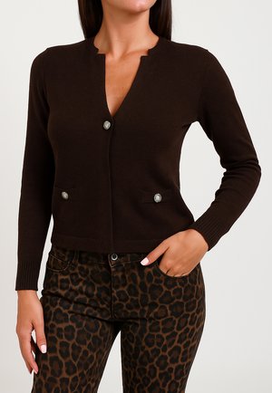 Cardigan marrone scuro con scollatura a V, due tasche frontali e dettagli in bottoni argentati. Indossato su pantaloni a stampa leopardata. Texture a maglia liscia.