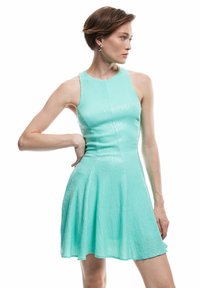 Un vestito senza maniche verde menta con gonna a campana, realizzato in un tessuto testurizzato che presenta un leggero luccichio e una scollatura rotonda.