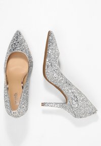 Chaussures à talons hauts argentées pailletées avec un design à bout pointu. Doublure intérieure beige lisse et semelle extérieure brune. Surface scintillante avec une finition texturée.