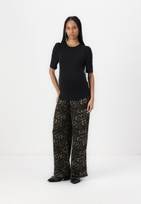 Crna majica kratkih rukava u kombinaciji s hlačama širokog kroja s smeškim leopard printom. Model stoji na jednobojnoj pozadini.