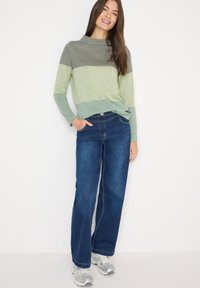 Hellgrün-schwarzes, gestreiftes Langarmshirt mit lockerer Passform, kombiniert mit dunkelblauen Jeans mit weitem Bein und silbernen Sneakers.