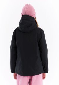 Zwarte waterdichte jas met capuchon, voorzien van elastische manchetten en een reflecterend logo op de schouder, naast een roze gebreide muts en broek.