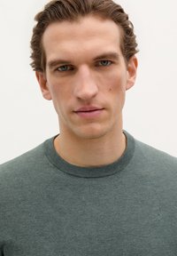 Pull en maille verte avec une finition texturée, col rond et poignets côtelés. Design minimaliste avec un subtil logo au niveau de la poitrine.
