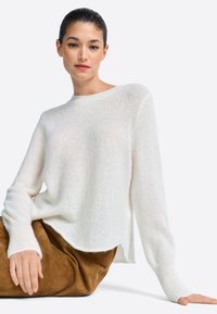 Beli pleten pulover s krožnim izrezom, dolgimi rokavi in sproščenim pristopom. Mehak, prosojen tekstura. Združeno s rjavim semišnim krilom.