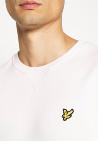 Felpa rosa chiaro con collo rotondo, dotata di un piccolo logo ricamato di un uccello giallo e nero sul petto e dettagli di cucitura testurizzata.