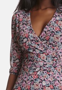 Květinové šaty s hlubokým véčkovým výstřihem, detaily na nařasených rukávech a kombinací růžových, modrých a krémových květin na tmavém pozadí.