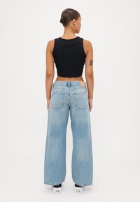 Top cropped preto, jeans de perna larga azul claro e sapatilhas pretas. Os jeans têm uma cintura alta e bolsos traseiros.