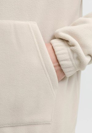 Hand inserted into the pocket of a cream-colored fleece jacket with elastic cuff visible on the wrist.