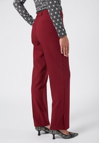 Bordowe spodnie o dopasowanym kroju z prostymi nogawkami, kieszeniami bocznymi i gładką teksturą materiału, zestawione z butami w czarno-białe wzory.