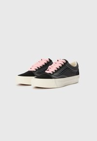 Black suede sneakers with pink laces, white rubber soles, and contrasting stitching. Classic low-top design. Smooth texture, rounded toe shape.