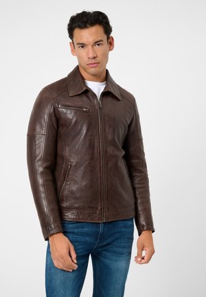 Brown leather jacket with a straight cut, zippered pockets, and a collar, paired with blue jeans. Smooth texture and structured design.